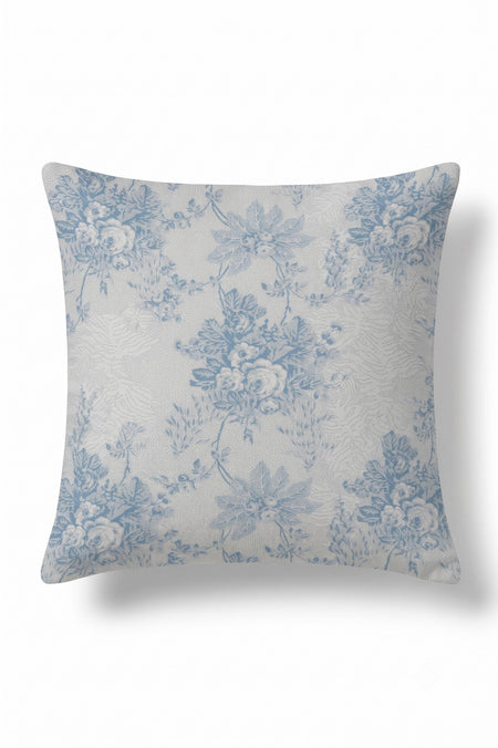 A square throw pillow featuring a classic blue floral toile de Jouy pattern on a textured off-white background, shown against a plain white studio backdrop.