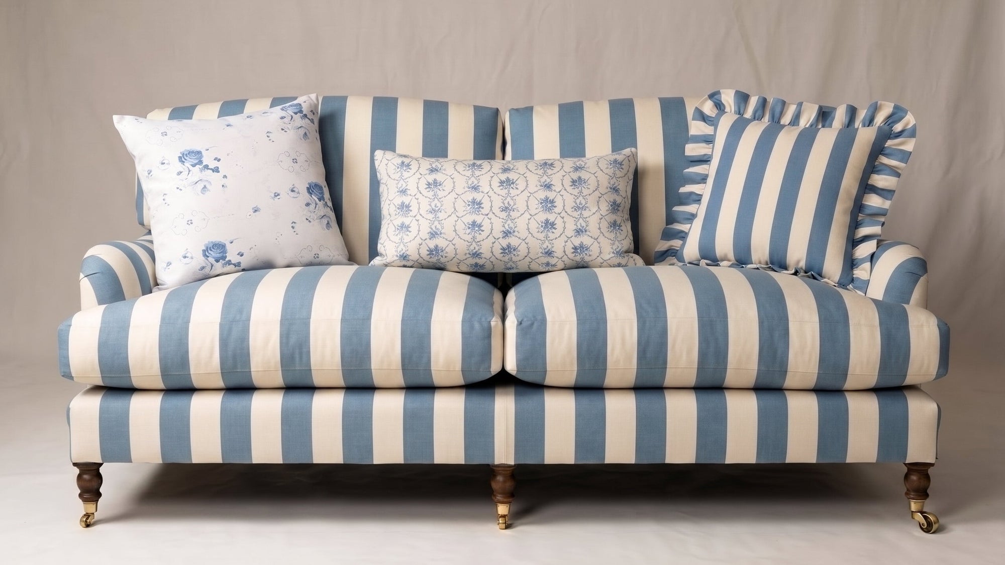 A classic English style sofa with blue and cream vertical stripes, styled with four decorative throw pillows, set against a neutral studio backdrop.